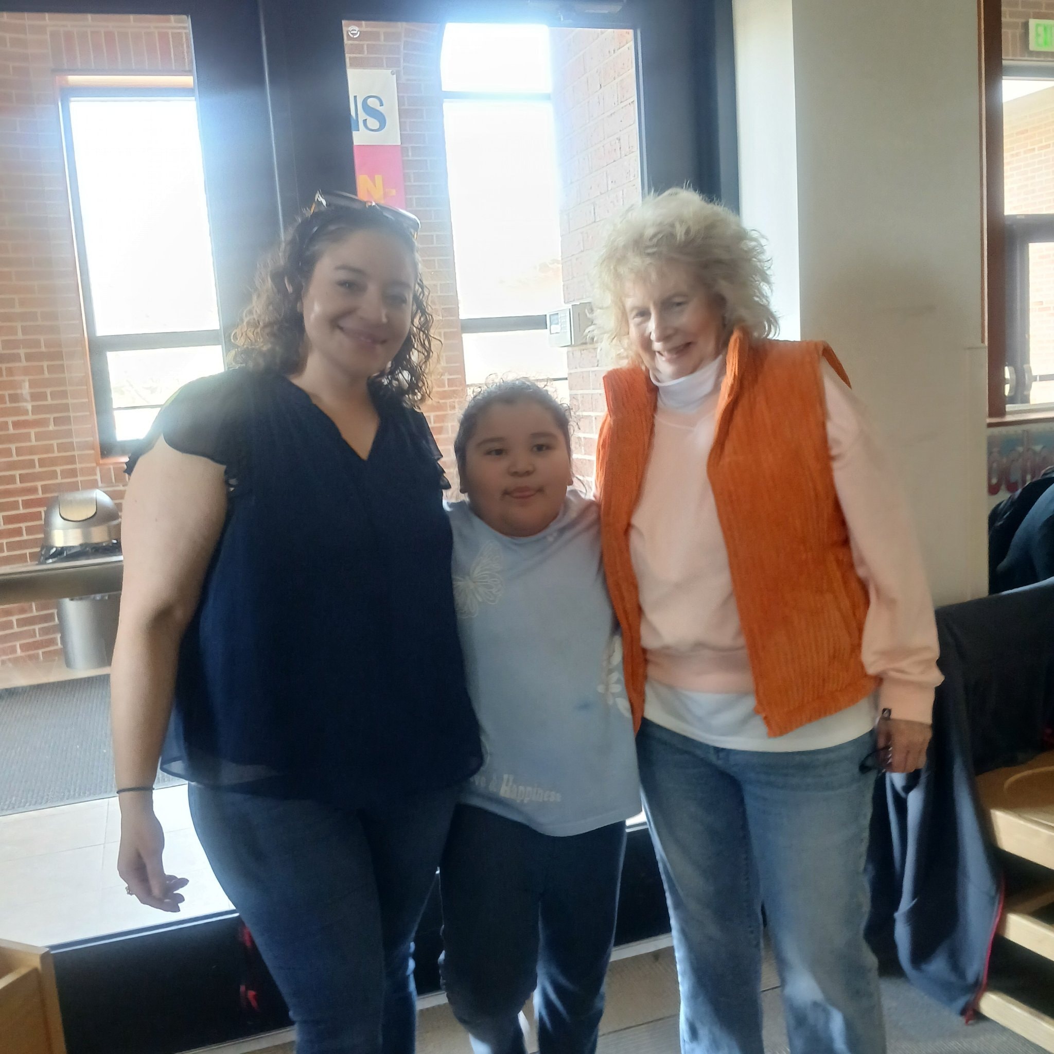 Three community members posing together indoors with brick walls and bright windows